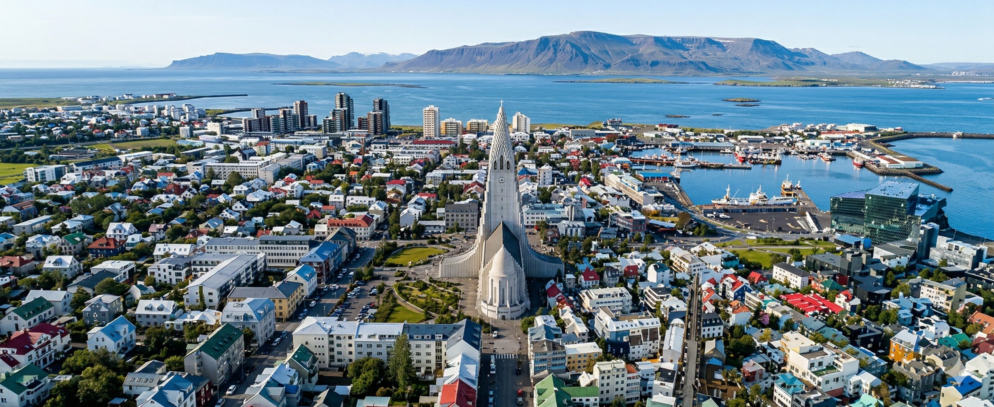 Sweepingly high panoramic aerial photograph of Reykjavik, Iceland, with the iconic Hallgrimskirkja stepped spire dominating.