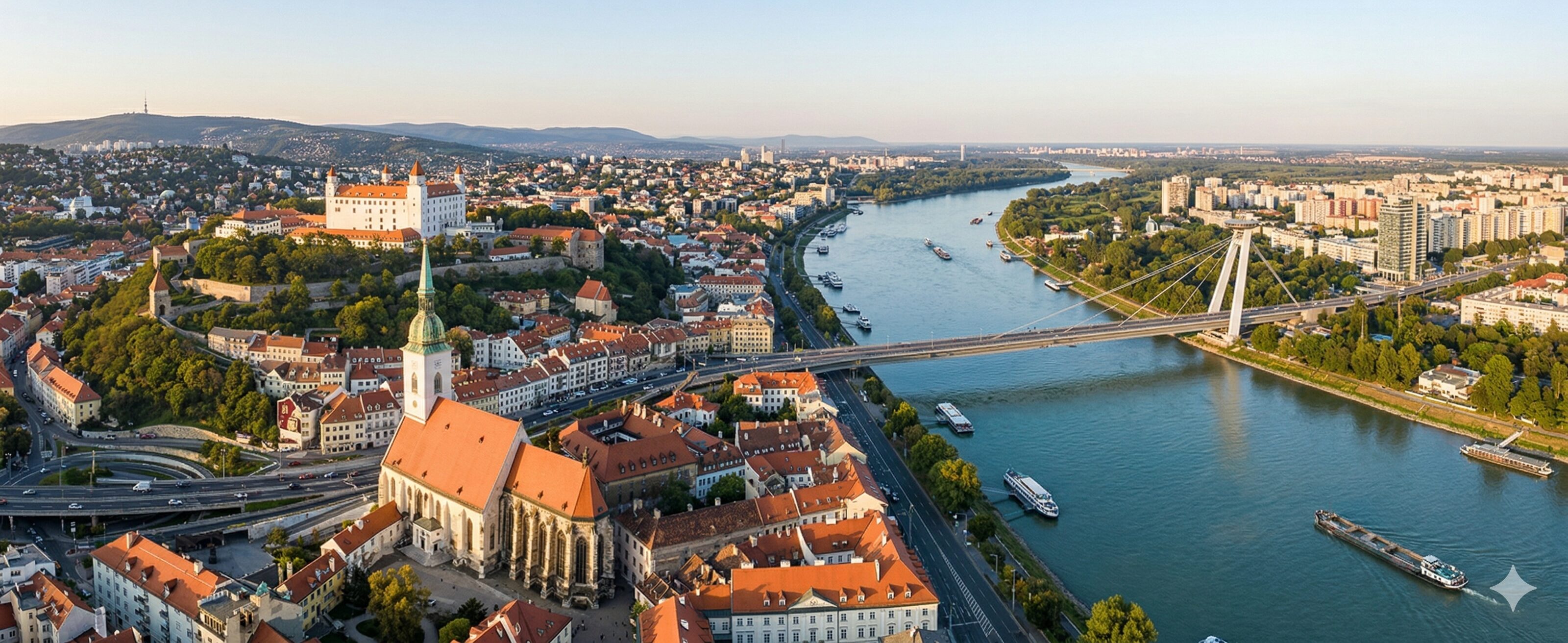 Wide panoramic aerial photograph of Bratislava, Slovakia, taken from a high altitude at golden hour.